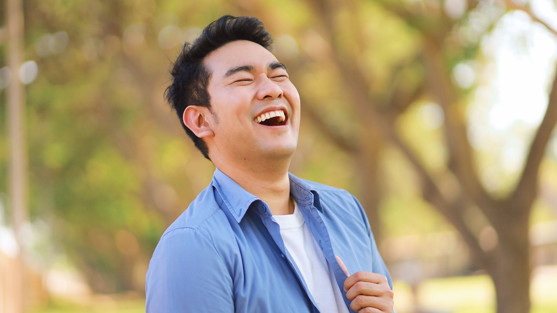 Man in blue shirt laughing outdoors.